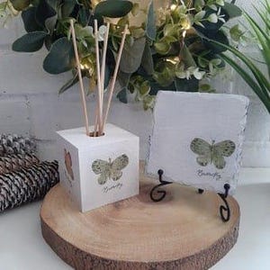 Könnte beinhalten: Ein weißer Holzwürfel mit einem Schmetterlingsdesign und einem Loch für Stäbchen. Ein weißer quadratischer Schieferuntersetzer mit einem Schmetterlingsdesign und dem Wort "Butterfly" darauf. Beide Artikel haben ein grünes Schmetterlingsdesign.