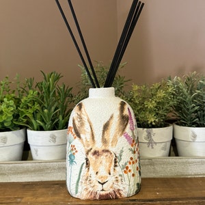 May include: White ceramic diffuser bottle with a brown rabbit illustration and floral accents. Black diffuser sticks are in the bottle.