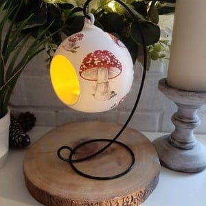May include: White ceramic hanging candle holder with a mushroom design. The holder has a cut-out circle in the front for a tea light candle.