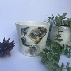 May include: White ceramic planter featuring a black and white illustration of a dog's face. The dog has brown markings on its face and is looking to the left.