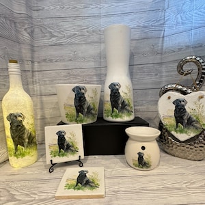 Könnte beinhalten: Ein Set von Dekorationsartikeln mit einem schwarzen Labrador Retriever. Das Set beinhaltet eine Flasche, eine Vase, einen Blumentopf, einen Untersetzer, einen Wachsschmelzer und eine herzförmige Plakette. Alle Artikel sind weiß mit einem Bild eines schwarzen Labrador Retrievers.