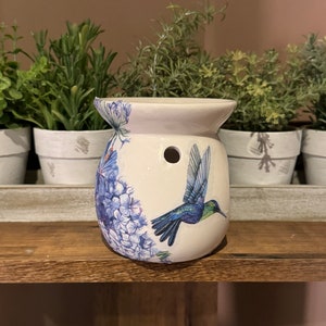 Puede incluir: Difusor de aceite de cerámica blanca con un diseño floral azul y blanco y un colibrí en vuelo. El difusor tiene un agujero en la parte superior para agregar aceites esenciales.