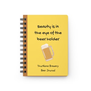 May include: Yellow spiral bound notebook with the text "Beauty is in the eye of the beer holder" and a cartoon illustration of a beer mug. The bottom of the notebook says "YourName Brewery Beer Journal".