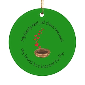 Op de afbeelding: Een ronde, groene keramische ornament met een gouden touwtje om op te hangen. Het heeft een bruin nest met rode hartaccenten en de tekst "My Empty Nest just shows how well my brood has learned to fly."