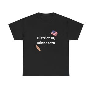 May include: Black t-shirt with the text "District 13, Minnesota" in white, an American flag graphic, and a hand gesture. The shirt is a classic crew neck style.