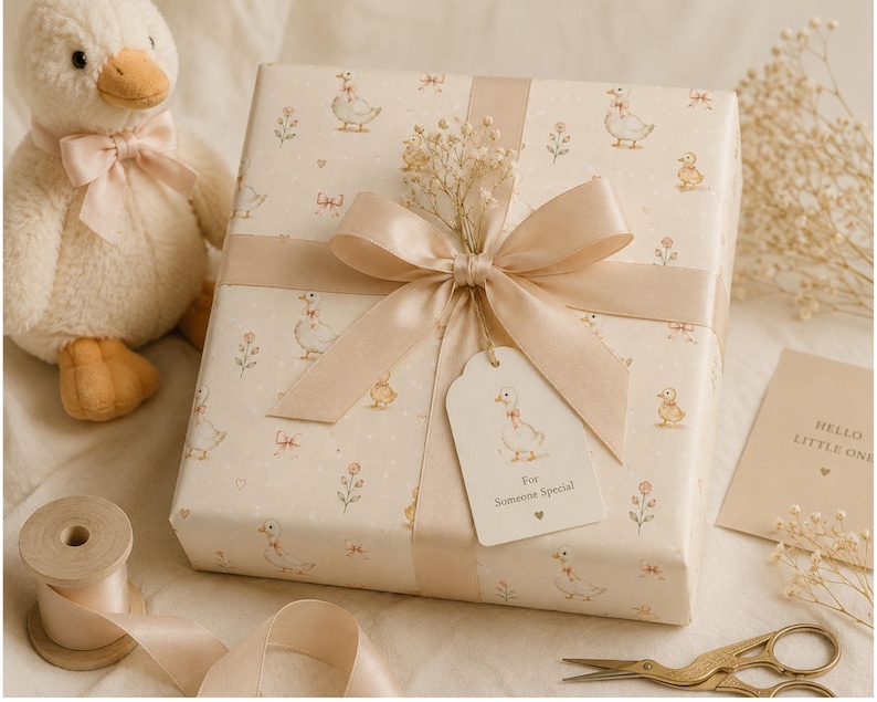 May include: A square gift box wrapped in cream paper with a repeating pattern of small ducks and flowers, tied with a beige satin ribbon. A gift tag attached to the ribbon reads "For Someone Special" with a small heart icon below the text.