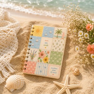 May include: A spiral-bound notebook featuring a grid of nine square illustrations including a sun, sailboats, a palm tree, flowers, and text that reads "sun sea smile" and "sunshine state of mind" with small heart icons on a sandy surface.