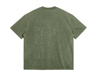 Puede incluir: Camiseta verde oliva con el texto blanco "IT'S TIME FOR MATCHA" en letras retro. La camiseta tiene un aspecto vintage y un cuello redondo clásico.