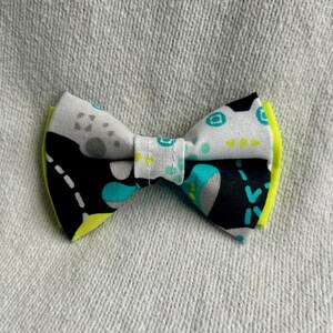 May include: A black, white, and turquoise bow tie with a neon yellow trim. The bow tie has a geometric pattern.