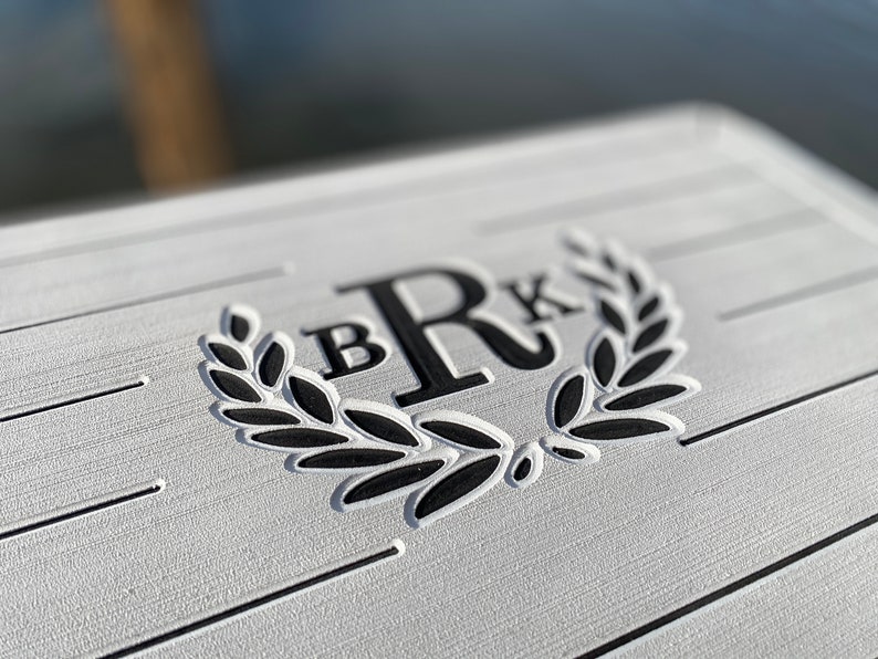 May include: Close-up of a white, textured surface with horizontal lines. The surface features a black laurel wreath design with the letters "B" and "R" and "K" in a bold, sans-serif font. The design is likely for a personalized item.
