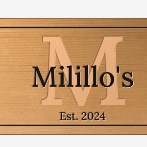 May include: A wooden sign with a raised, gold-colored letter "M" and the text "Milillo's Est. 2024".