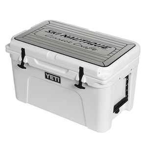 Puede incluir: Nevera blanca Yeti con tapa negra y un logotipo gris de Ski Nautique Correct Craft en la parte superior. La nevera tiene un logotipo negro de Yeti en el lateral.