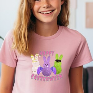 Può includere: Maglietta rosa con una grafica di tre Peeps di Pasqua vestiti da personaggi di Halloween. Il testo "Hoppy Easterween" è stampato sotto i Peeps.