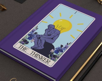 Peut inclure: Un carnet violet avec un design de carte de tarot représentant un homme qui réfléchit avec une ampoule au-dessus de sa tête. La carte indique "The Thinker" et "I".