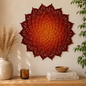 May include: A circular crochet wall hanging featuring a vibrant gradient of warm colours, transitioning from a bright orange centre to deep burgundy red at the outer edges, with intricate petal-like patterns and delicate lace-like stitching throughout.