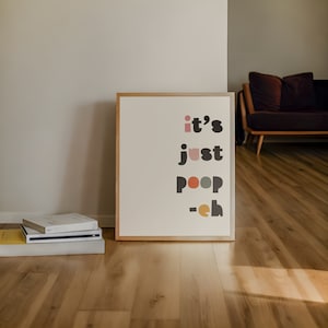 May include: A framed print with the text "it's just poop - eh" in black and white with colorful accents. The print is hanging on a white wall in a room with hardwood floors.