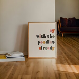 Könnte beinhalten: Ein gerahmter Druck mit dem Text "oy with the poodles already" in einer bunten, geometrischen Schriftart. Der Druck ist auf einem hellbeigen Hintergrund und hat einen Holzrahmen.