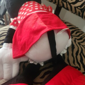 May include: A large plush toy of a cartoon mouse wearing a red dress with white polka dots. The mouse is sitting on a zebra-print fabric.