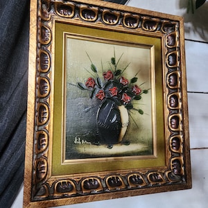 May include: A framed oil painting of a bouquet of red roses in a black vase. The painting is signed "Kilem" in the bottom left corner.