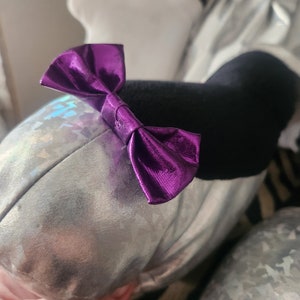May include: A silver plush toy with a purple bow. The toy has a holographic iridescent finish.