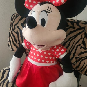 May include: A plush toy of Minnie Mouse wearing a red dress with white polka dots and a red bow with white polka dots.