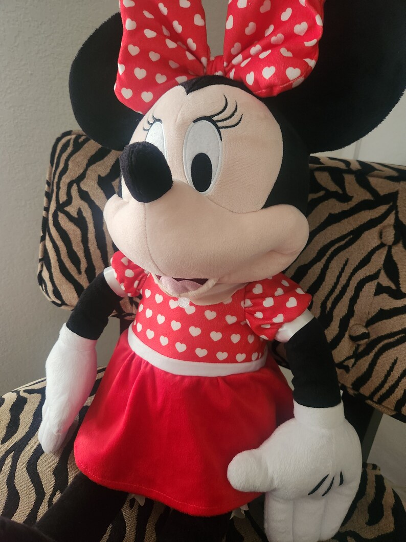 May include: A plush toy of Minnie Mouse wearing a red dress with white polka dots and a red bow with white polka dots.