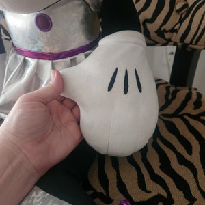 May include: A silver and black plush toy with a white glove. The glove has three black stitches on it.