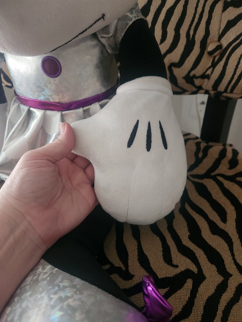 May include: A silver and black plush toy with a white glove. The glove has three black stitches on it.