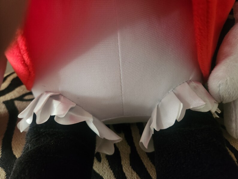 May include: A plush toy with a red and white dress and white ruffled trim. The toy is sitting on a striped fabric.