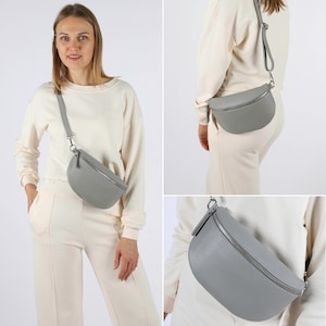 Könnte beinhalten: Eine graue Leder-Bauchtasche mit einem silbernen Reißverschluss und einem verstellbaren Riemen. Die Tasche wird über der Schulter getragen.