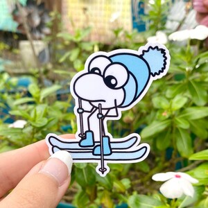 May include: A white cartoon character wearing a blue hat and blue ski boots is skiing on two blue skis. The character has large black eyes and a white body.