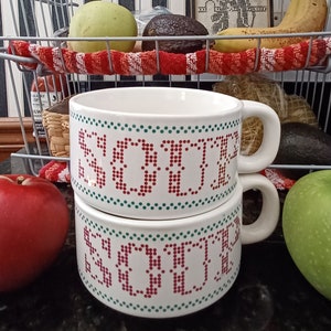 May include: Two white ceramic soup bowls with a red and green pixelated design that says "Soup" on them. The bowls are stacked on top of each other.