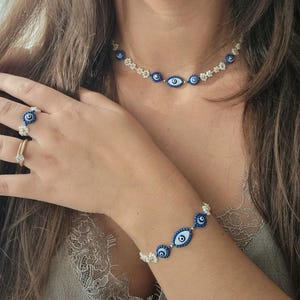 May include: A set of white and blue beaded jewellery featuring evil eye charms. The set includes a choker necklace and a bracelet.