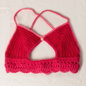 May include: A pink and red crocheted crop top with a scalloped hem and a button closure in the center.