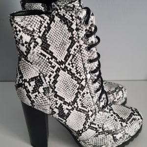 Puede incluir: Botines de tacón alto con estampado de piel de serpiente en blanco y negro. Los botines tienen cordones negros, un tacón negro grueso y una suela de plataforma. Los botines están hechos de un material texturizado. El tacón mide unos 10 cm.