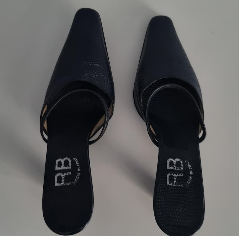 Pu&ograve; includere: Un paio di mules blu navy a punta con un motivo strutturato simile alla pelle di serpente. Le scarpe hanno un tacco basso e un cinturino sulla parte superiore del piede. Le suole sono contrassegnate con "RB" e "MADE IN ITALY".