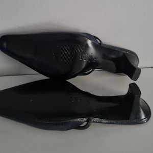 Pu&ograve; includere: Paio di mules nere con tacco. Le scarpe hanno la punta a punta e un piccolo tacco. Le suole sono strutturate. Le scarpe sono realizzate in un materiale lucido.