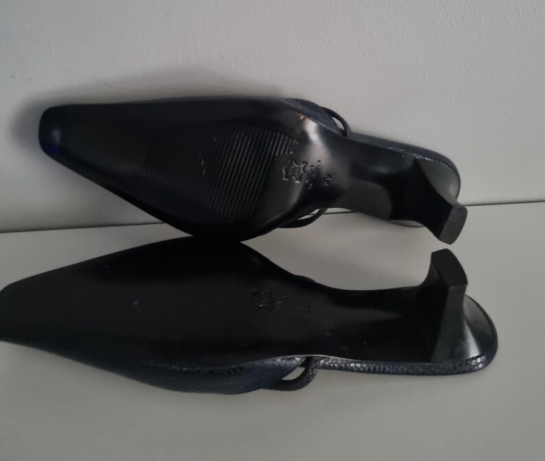 Pu&ograve; includere: Paio di mules nere con tacco. Le scarpe hanno la punta a punta e un piccolo tacco. Le suole sono strutturate. Le scarpe sono realizzate in un materiale lucido.