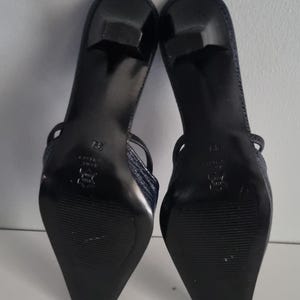 Pu&ograve; includere: Un paio di sandali con tacco blu navy. Le scarpe hanno un motivo strutturato, simile alla pelle di serpente, sui cinturini e sulla tomaia. Le suole sono nere e i tacchi sono alti circa 5 cm.