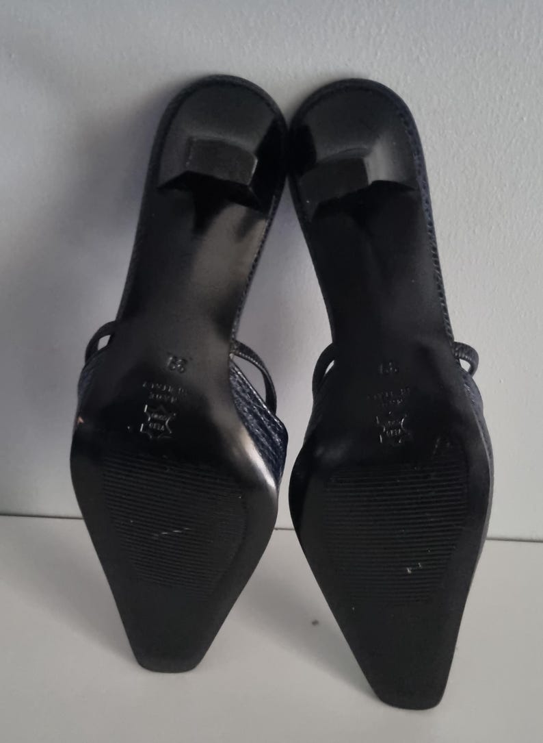 Pu&ograve; includere: Un paio di sandali con tacco blu navy. Le scarpe hanno un motivo strutturato, simile alla pelle di serpente, sui cinturini e sulla tomaia. Le suole sono nere e i tacchi sono alti circa 5 cm.