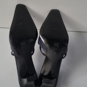 Pu&ograve; includere: Un paio di sandali con tacco blu navy. I sandali hanno la punta affilata e un sottile cinturino. Le suole sono nere con un motivo strutturato. I tacchi sono alti circa 5 cm.