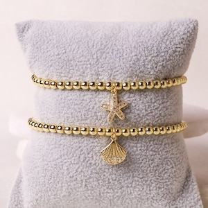 Op de afbeelding: Drie gouden kralen armbanden met een zeester en schelp bedel. De bedels zijn bezet met heldere strass steentjes.