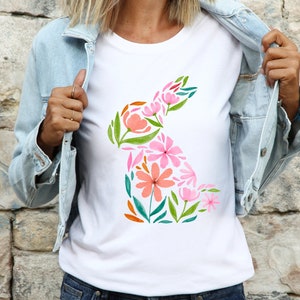 May include: A white t-shirt with a floral design in the shape of a rabbit. The flowers are pink, orange, green, and blue.