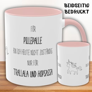 Könnte beinhalten: Weiße Keramiktasse mit rosafarbenem Rand und Henkel. Die Tasse hat schwarzen Text, der lautet "FÜR PILLEPALLE BIN ICH HEUTE NICHT ZUSTÄNDIG. NUR FÜR TRALLALA UND HOPSASSA". Die Rückseite der Tasse zeigt eine schwarze Strichzeichnung eines Einhorns mit einem Herzen auf der Flanke.