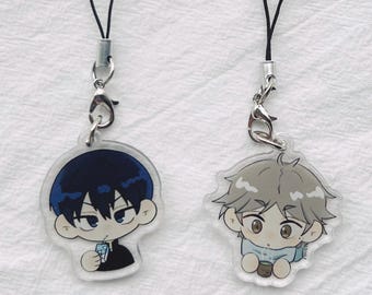 May include: Two anime-style character charms with black lanyards. One charm features a character with dark blue hair and a black outfit, holding a small item. The other charm depicts a character with gray hair and a light blue outfit.