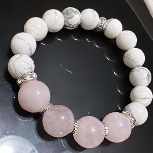 May include: A white and pink beaded bracelet with silver accents. The bracelet is made with white howlite beads and pink rose quartz beads.