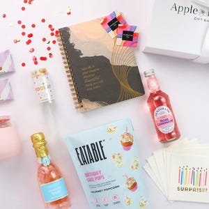 Flat lay showing inspirational journal, gourmet snacks, pink wine tumbler, birthday napkins, and party popper