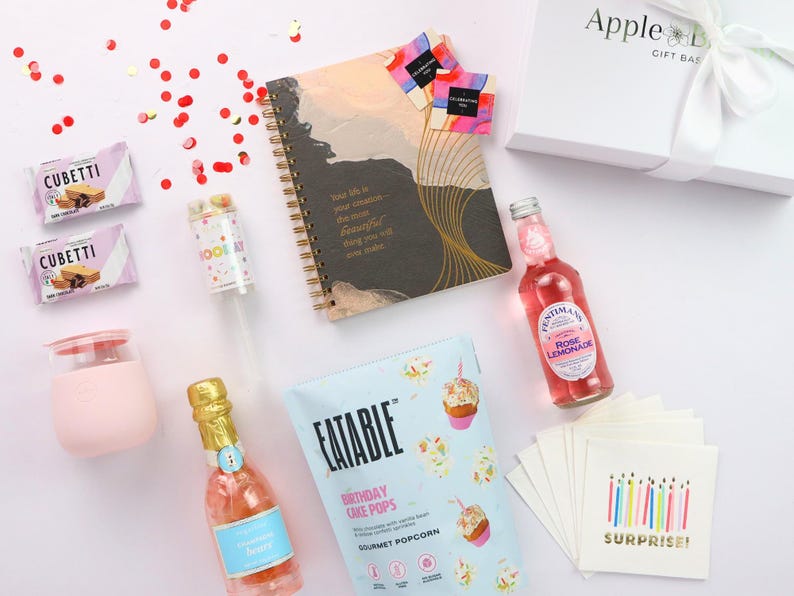 Flat lay showing inspirational journal, gourmet snacks, pink wine tumbler, birthday napkins, and party popper