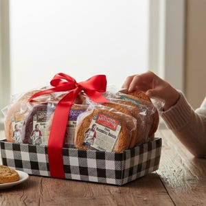 May include: A gift basket filled with packaged cookies and other treats, tied with a large red ribbon. The basket is black and white checkered. A plate of cookies sits in front of the basket.