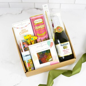 May include: A gift box containing a bottle of Martinelli's sparkling cider, a canister of Dolcetto strawberry rolled wafers, a box of Jocelyn & Co. mixed gummy bears, a tube of confetti, two yellow party blowers, and a gold sparkler.